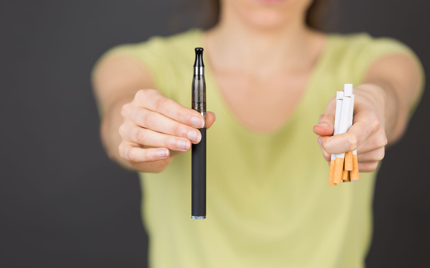 Foto af person der holder cigaretter og e-cigaret i hænderne