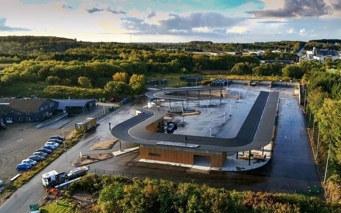 Luftfoto af Give Genbrugsplads omgivet af grønne områder og træer. Pladsen har en tydelig cirkulær rute for biler og adskillige containere og stationer til affaldssortering. Bygninger og overdækkede områder sikrer, at besøgende nemt kan navigere gennem genbrugspladsen.