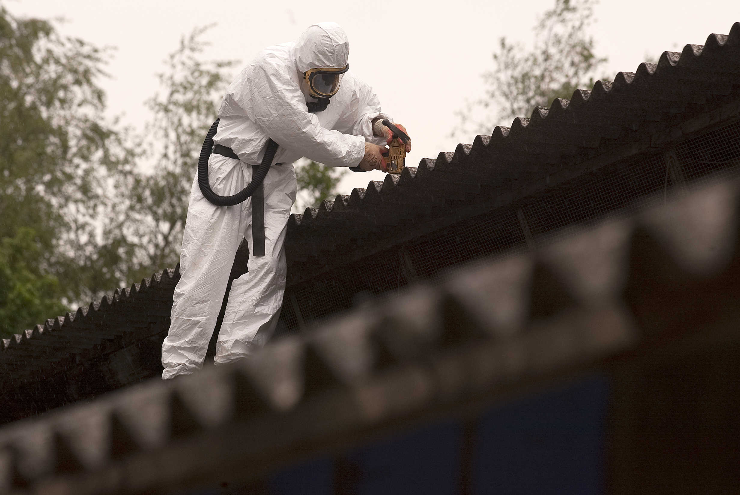 Person iført sikkerhedsudstyr og åndedrætsværn i færd med at renovere et asbest-tag.