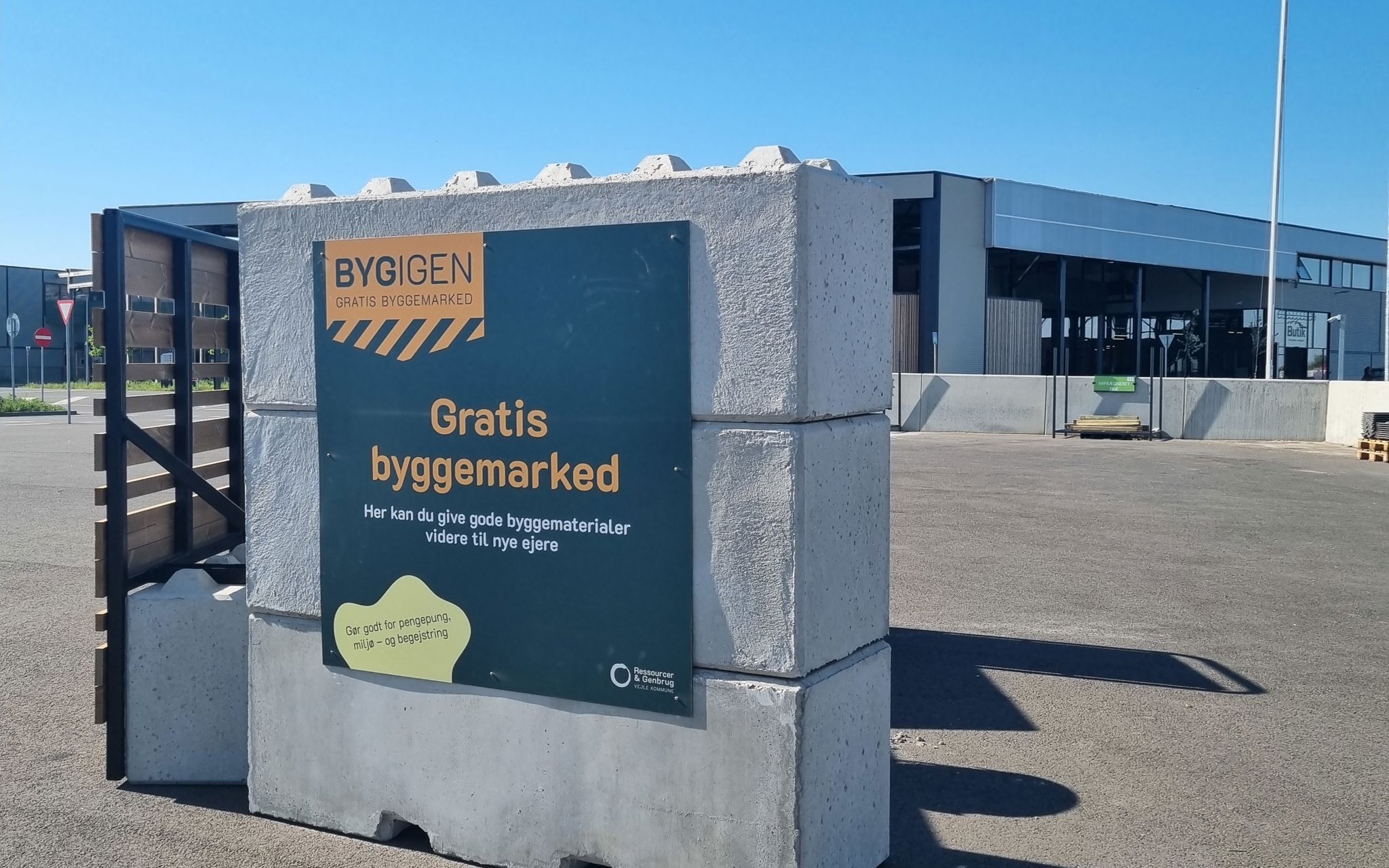 Skilt ved indgangen til BygIgen, et gratis byggemarked på RessourceCenter Vejle. Skiltet annoncerer "Gratis byggemarked" og inviterer borgere til at aflevere eller afhente gode byggematerialer, der kan genbruges.