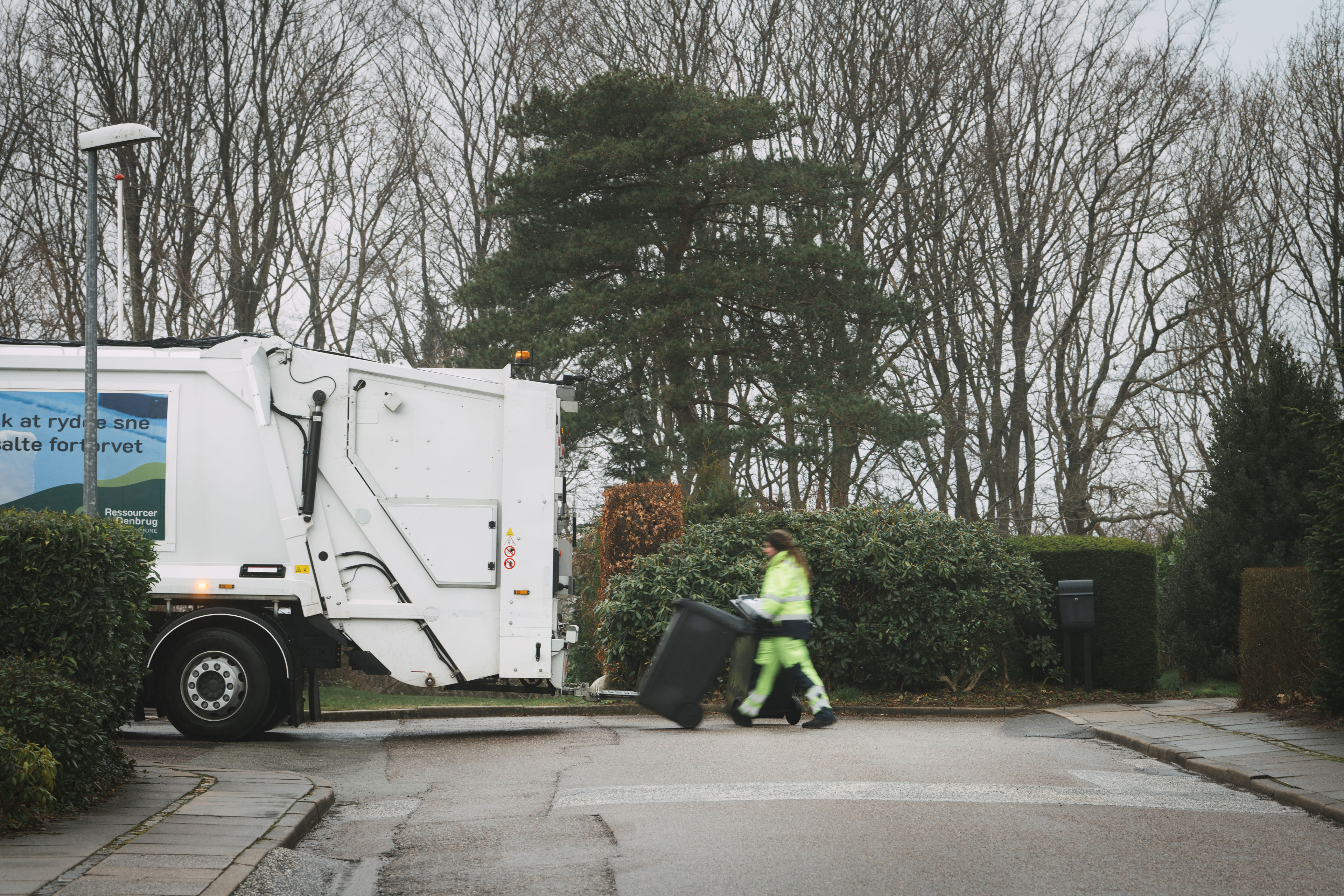 Skraldemand trækker en affaldsbeholder over vejen til skraldebilen på en stille villavej
