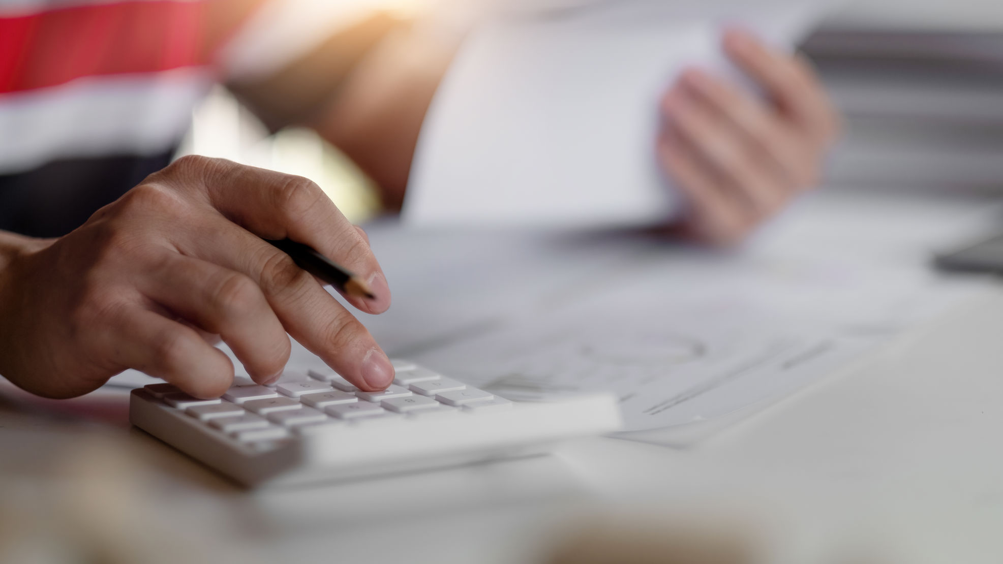Person bruger en lommeregner med den ene hånd, mens den anden holder et dokument.