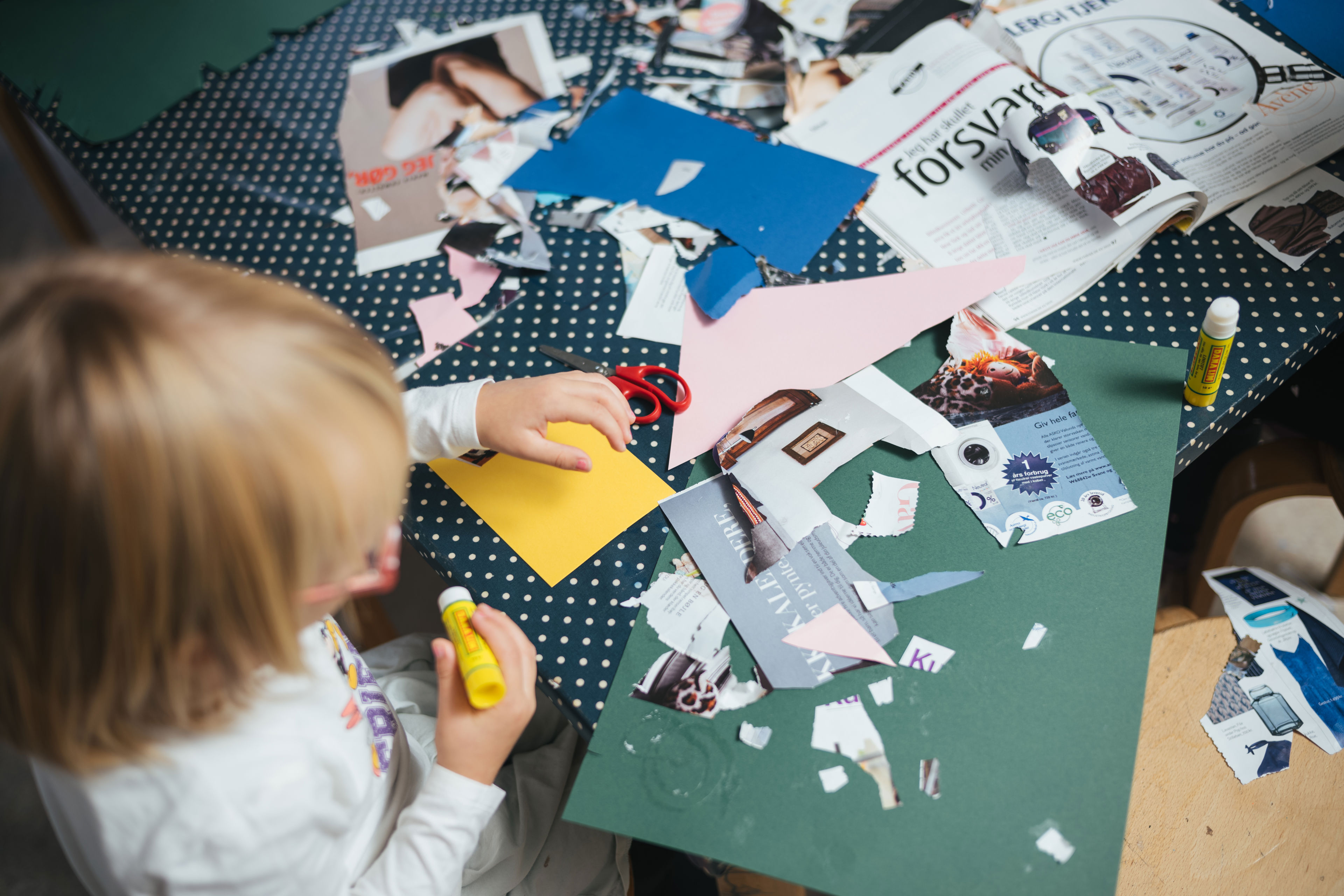 Barn sidder ved bord og klipper og klister i magasiner