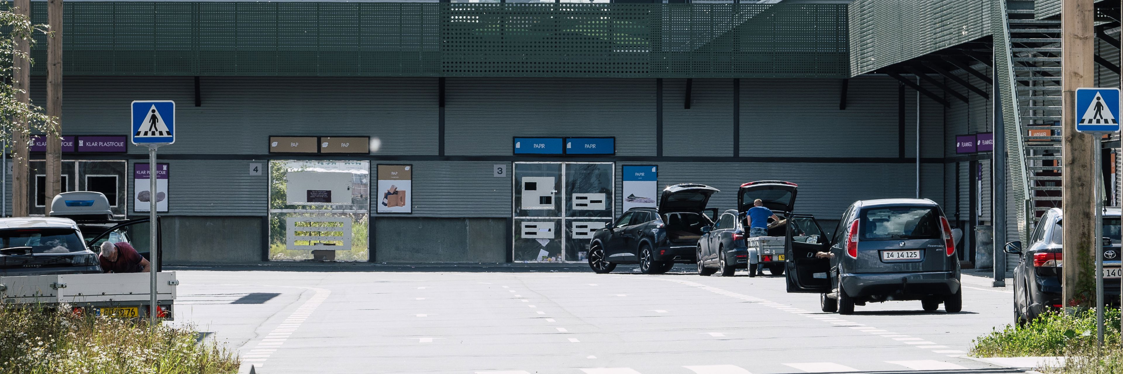 Genbrugspladsen ved RessourceCenter Vejle, hvor biler holder ved forskellige stationer for affaldssortering under et grønt overdække.