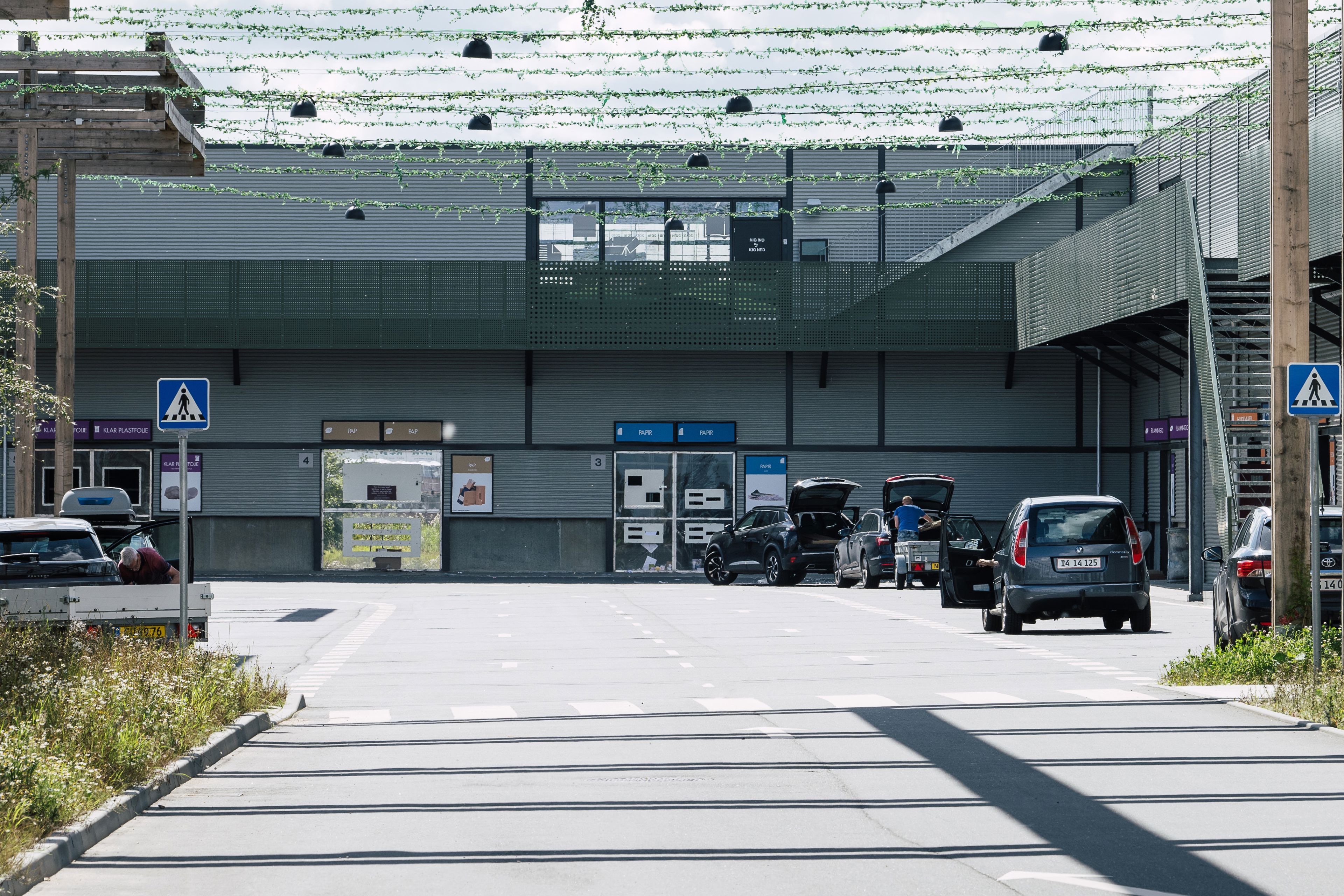 Genbrugspladsen ved RessourceCenter Vejle, hvor biler holder ved forskellige stationer for affaldssortering under et grønt overdække.