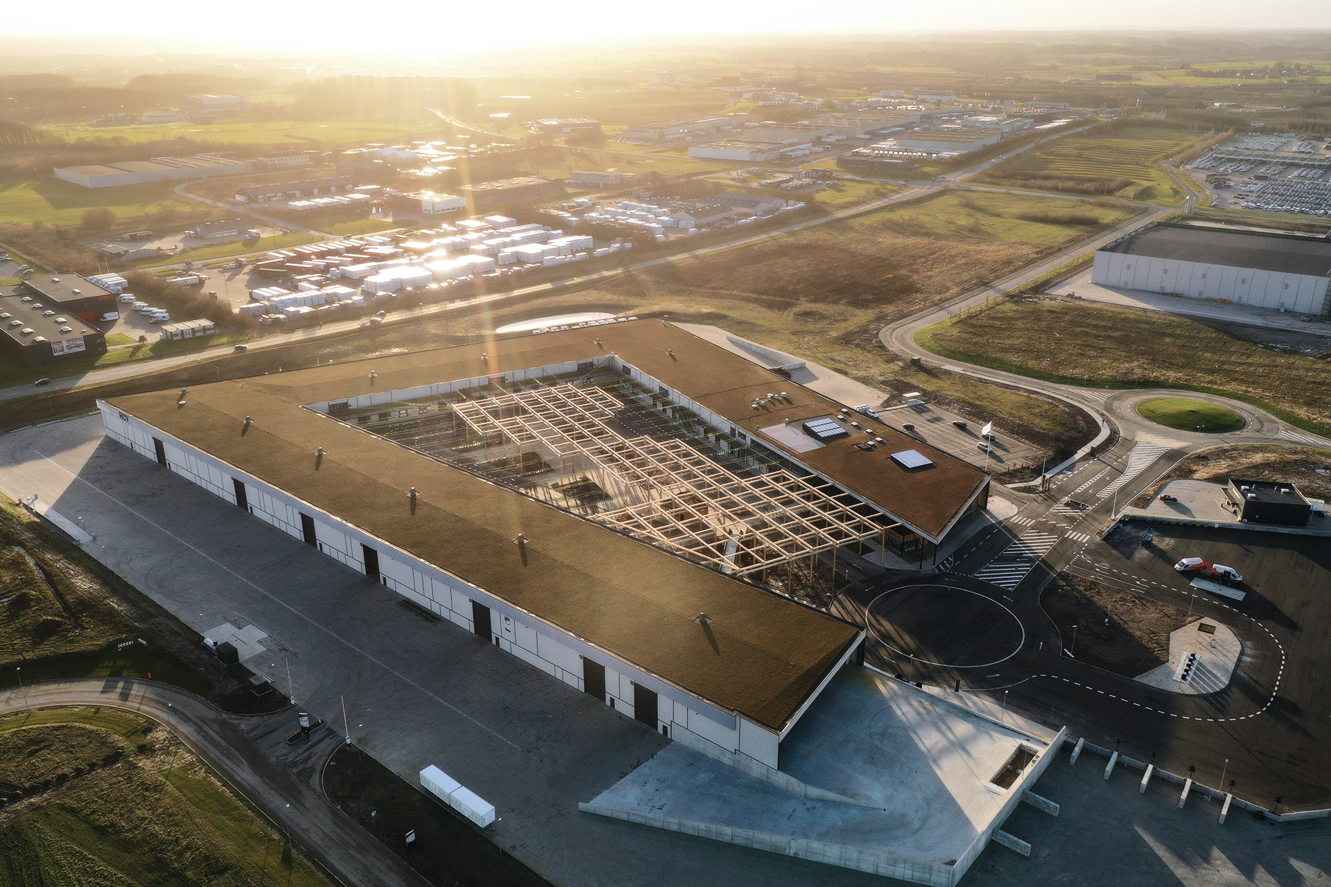 Dronefoto af RessourceCenter Vejle (RCV) med et grønt tag og solpaneler, omgivet af parkeringsplads og grønne områder, der viser centerets bæredygtige arkitektur og indre gårdstruktur.