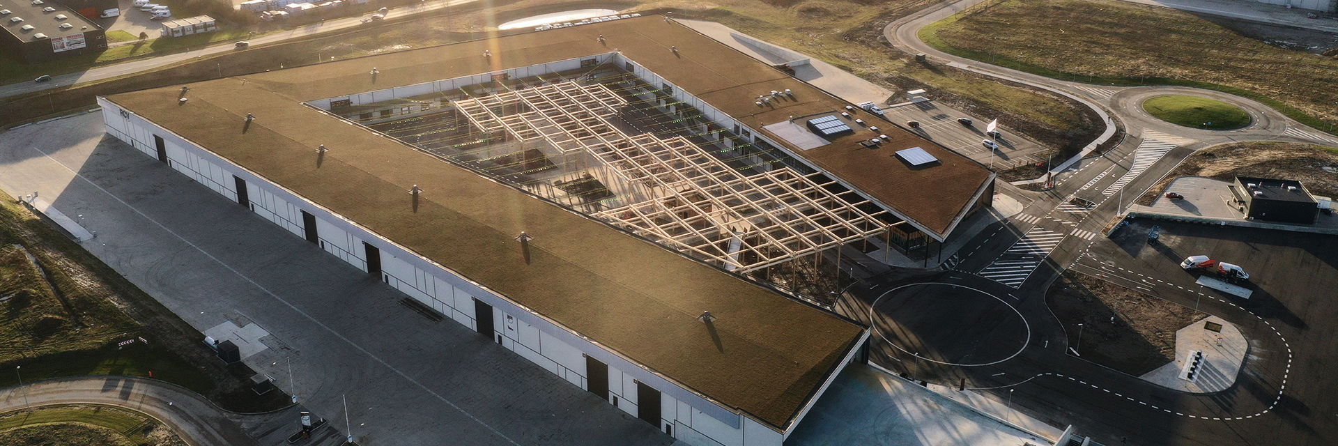 Dronefoto af RessourceCenter Vejle (RCV) med et grønt tag og solpaneler, omgivet af parkeringsplads og grønne områder, der viser centerets bæredygtige arkitektur og indre gårdstruktur.