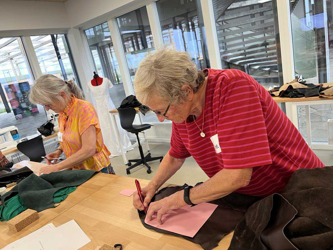 To ældre kvinder ved et arbejdsbord i Laboratoriet på RCV. I gang med at tegne og klippe sy-mønstre i stof.