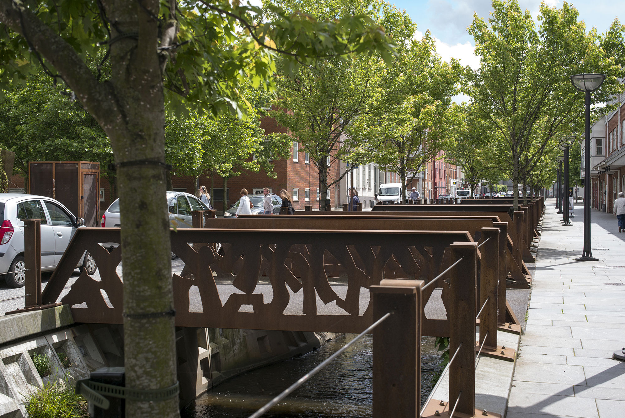 Dæmningen i Vejle med grønne træer, trafik og menneskemylder.
