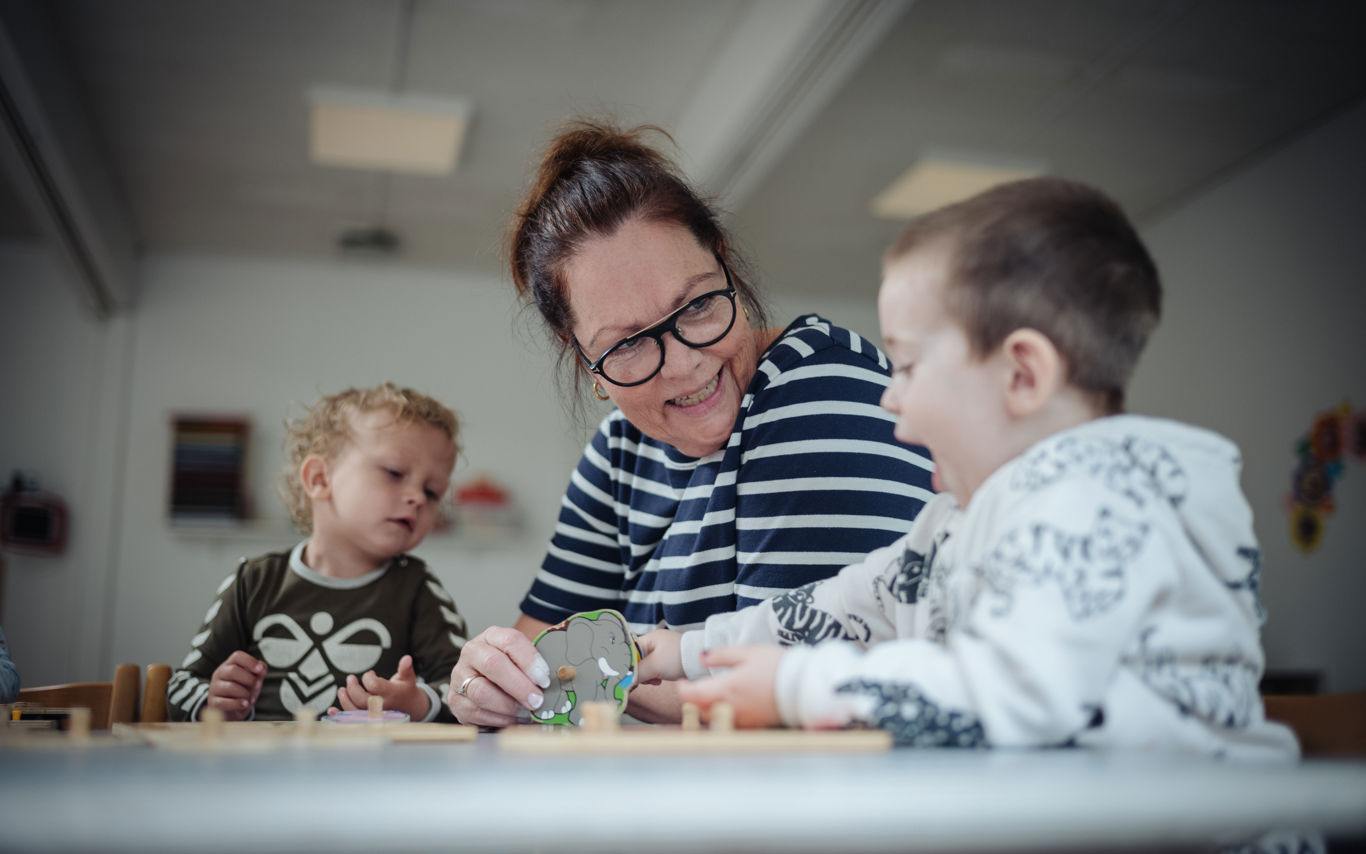 Pædagog og to børnehavedrenge leger med puslespil ved bordet