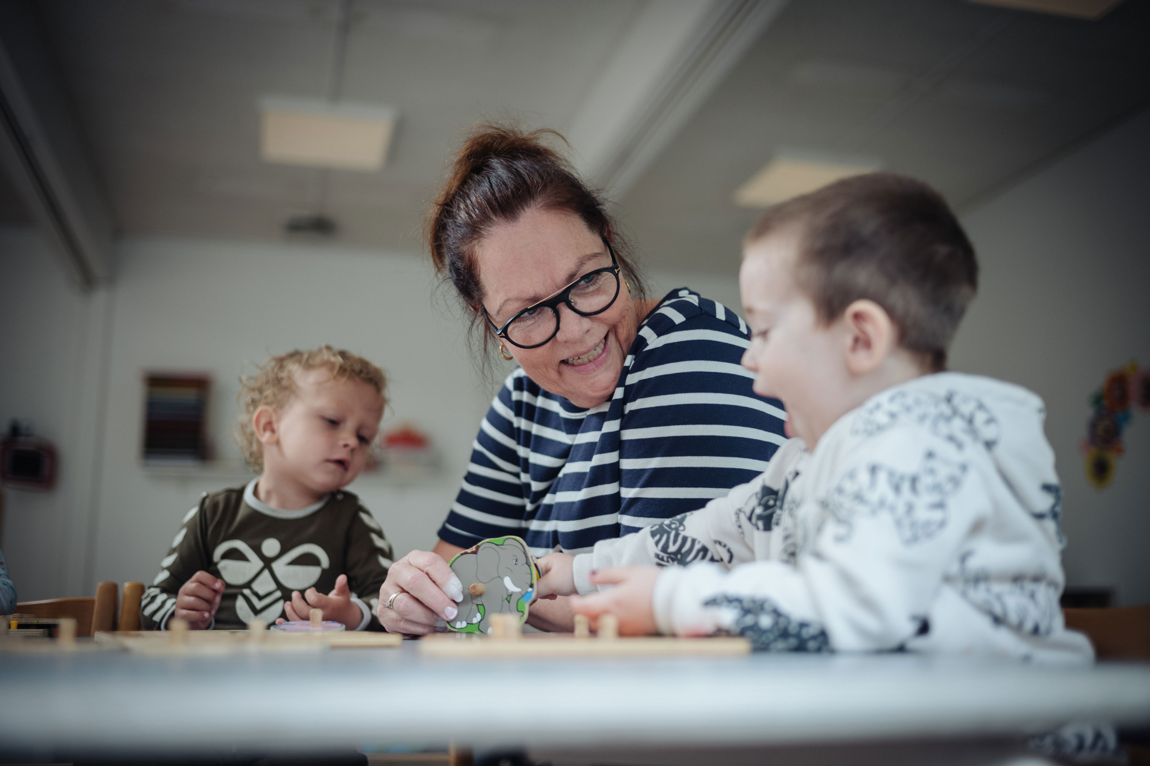 Pædagog og to børnehavedrenge leger med puslespil ved bordet