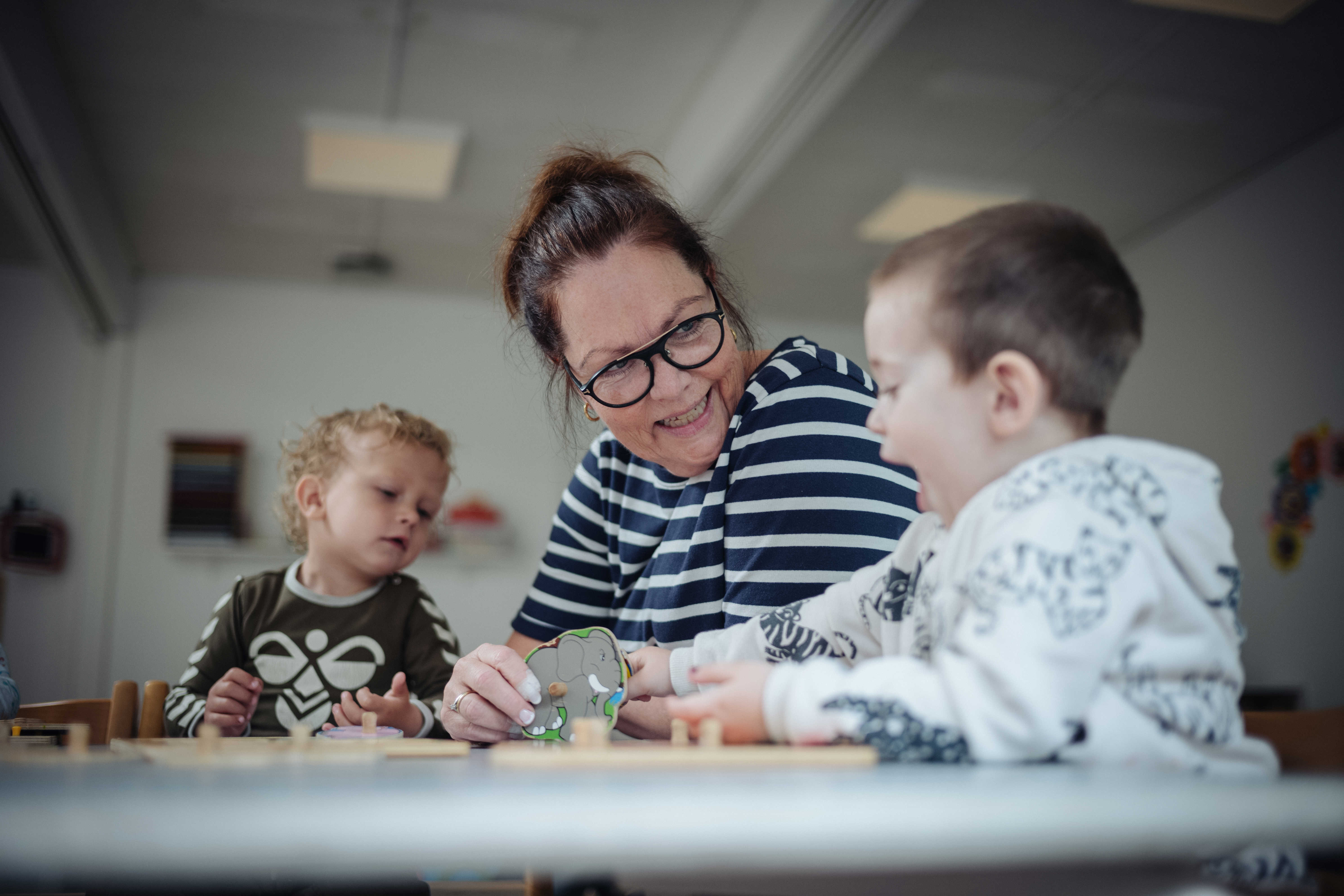 Pædagog og to børnehavedrenge leger med puslespil ved bordet